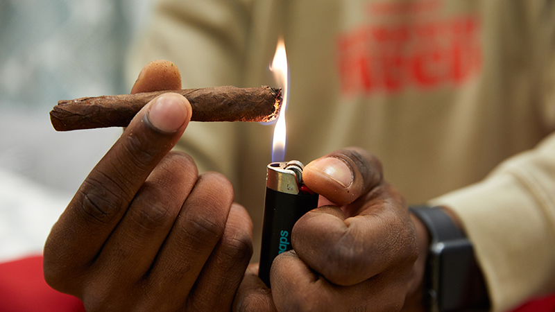 Close-up of a young black man lighting a blunt marijuana cigarette. 