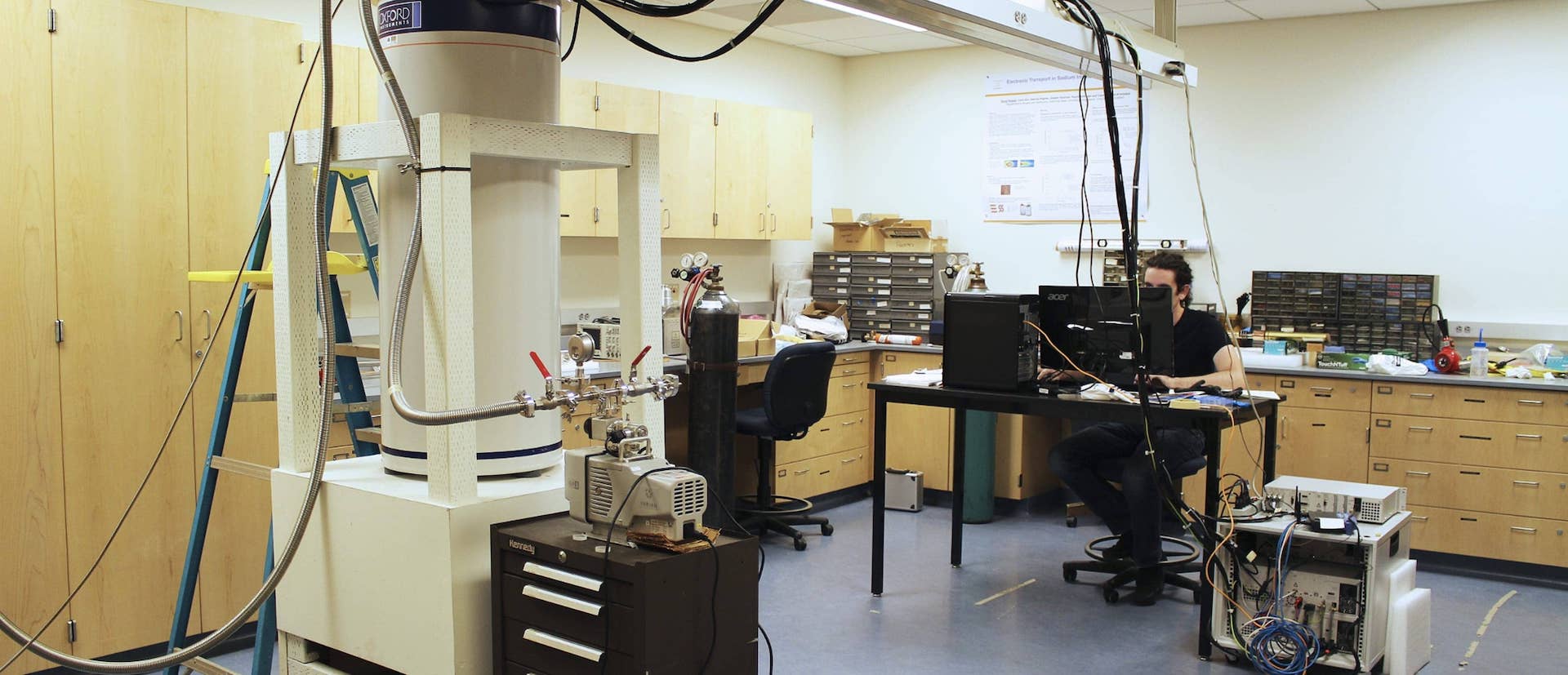 Person in a laboratory sat in front of a computer, surrounded by equipment