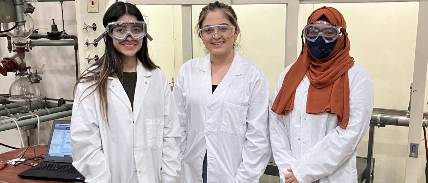 Three people wearing laboratory coats, protective goggles smiling