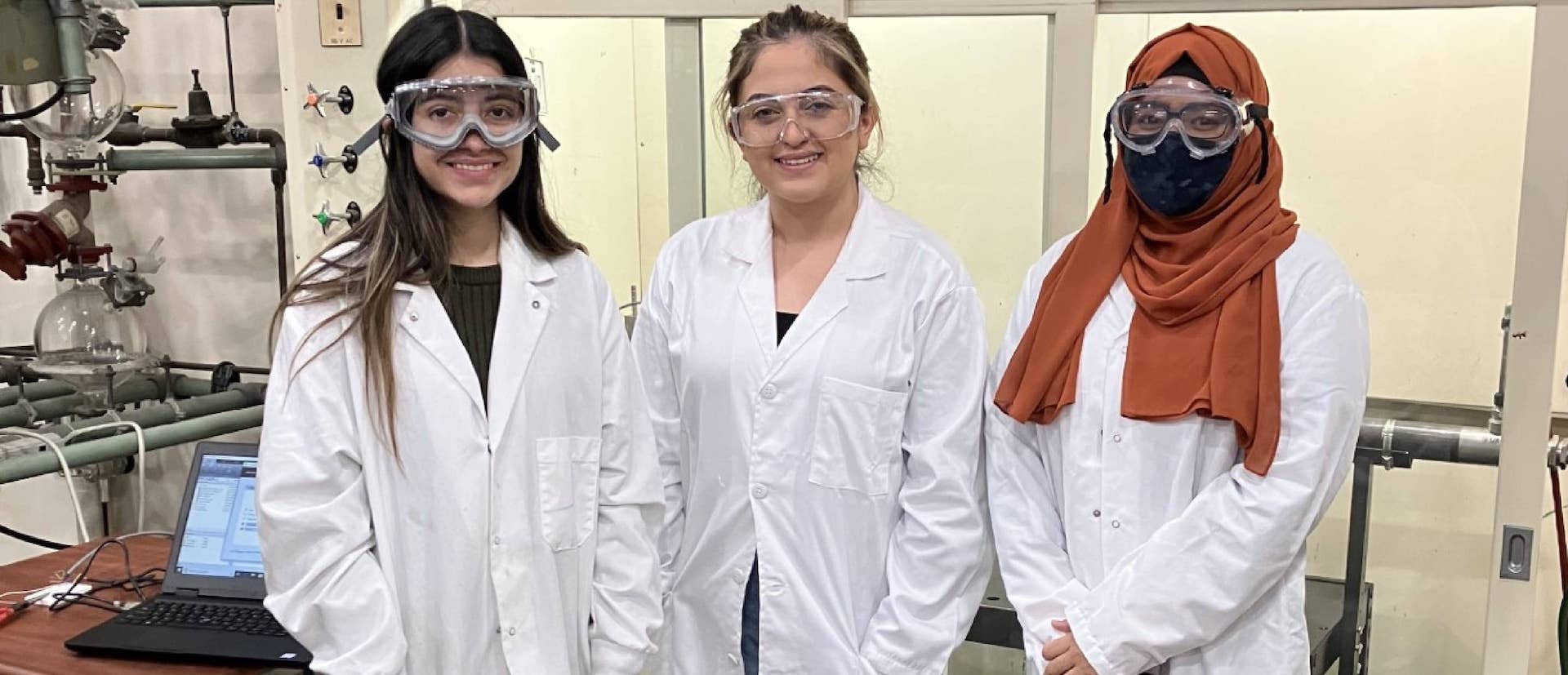 Three people wearing laboratory coats, protective goggles smiling