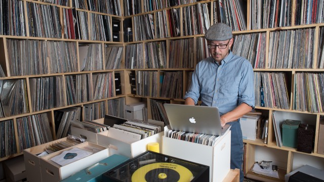 Photo of Oliver Wang in his studio full of floor-to-ceiling music vinyls.